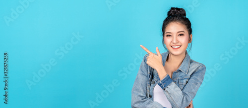 Banner of Happy asian woman standing pointing hands to copyspace on blue background. Cute asia girl smiling wearing casual jeans shirt and finger pointing to aside for present promotions.