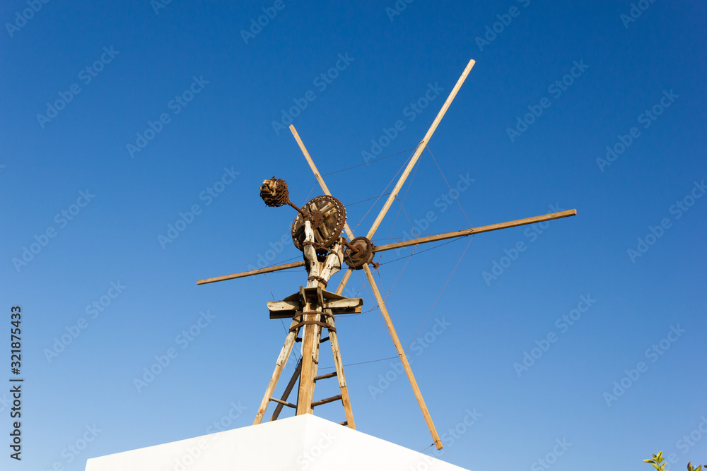 Old fashioned wooden windmill on top of building roof over blue sky. Antique technology in rural area Old fashioned wooden windmill on top of building roof over blue sky. Antique technology in rural area