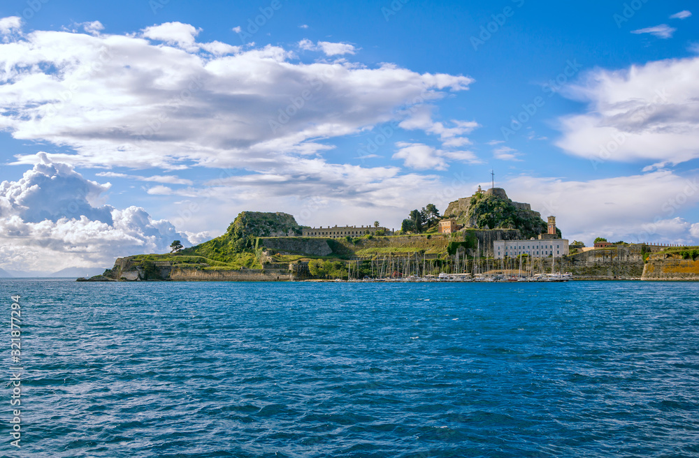 View of ancient venetian fortress at Corfu Island, Greece. Old stone walls, covered with green grass and moss, yachts on sea water surface and blue sky. 