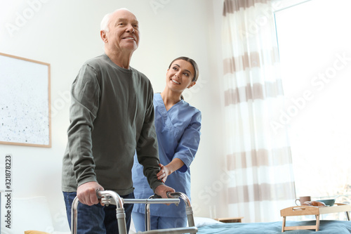 Care worker helping elderly man with walker in geriatric hospice