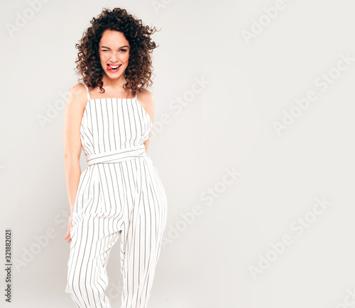 Portrait of beautiful smiling model with afro curls hairstyle dressed in summer hipster clothes.Sexy carefree girl posing in studio on gray background.Trendy funny and positive woman shows tongue
