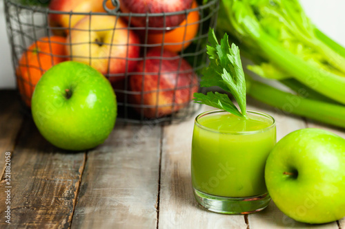 Healthy food, vegan diet concept - glass of fresh green juice or smoothie with celery, apple, orange. Antioxidant fresh detox beverage with raw ingredients. Close up, wooden background, copy space