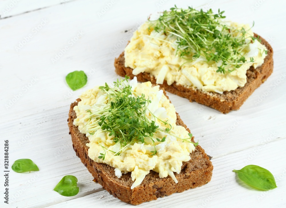 Egg salad over brown bread with garden cress. White background. Homemade spread made from eggs, mayonnaise and mustard. Egg salad over brown bread with garden cress. White background. Homemade spread made from eggs, mayonnaise and mustard.