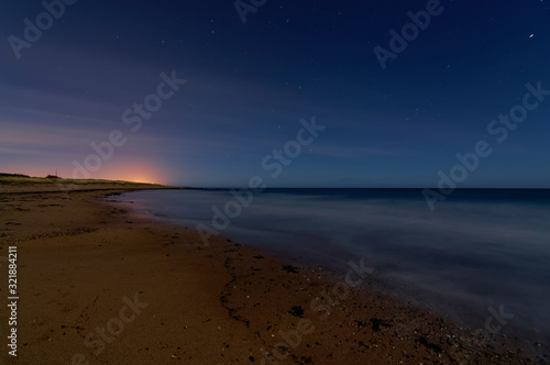 A long exposure night photograph of Easthaven beach with the tide out, and the lights of Arbroath seen above the horizon on a December Night. photo