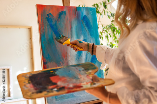 Female artist drawing acrylic painting on easel at her atelier