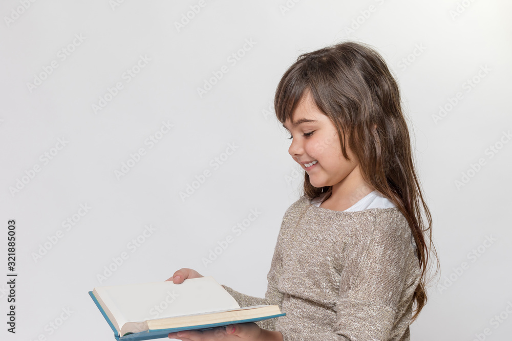 Side view of smiling long haired tanned little girl reading a book. Side view of smiling long haired tanned little girl reading a book.