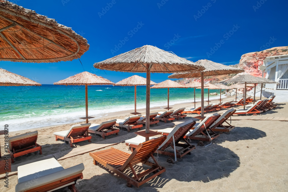 Amazing sandy beach landscape with chairs for relaxation and umbrellas on sunny day. Milos island on Aegean sea. Greece. Vacation in paradise concept