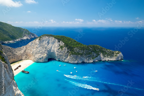 Picturesque top view of Navagio Beach or Shipwreck Beach. Old ship after crash on sand in lagoon surrounded by high rocks. Boats floating turquoise Ionian Sea. Paradise in Zakynthos island, Greece