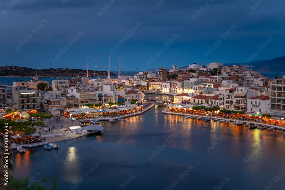 Beautiful sunset at Agios Nikolaos city, Port at Aegean sea. Crete,Greece. Peaceful harbor of Voulismeni Lake. Long promenade with restaurants.  Panoramic view of seaport with yachts and boats at quay