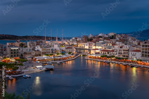 Beautiful sunset at Agios Nikolaos city  Port at Aegean sea. Crete Greece. Peaceful harbor of Voulismeni Lake. Long promenade with restaurants.  Panoramic view of seaport with yachts and boats at quay