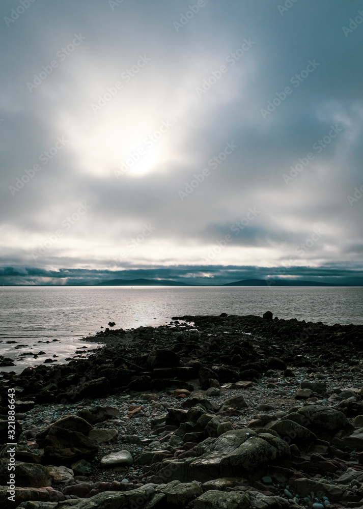 Rocky coastline and views over Galway Bay to the Burren with rainclouds over the mountains