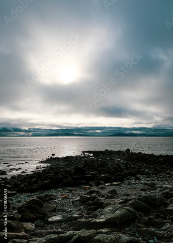 Rocky coastline and views over Galway Bay to the Burren with rainclouds over the mountains