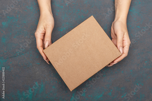 Female hands holding cardboard box with empty copy space topsheet over dark wooden background. © Galina_lya
