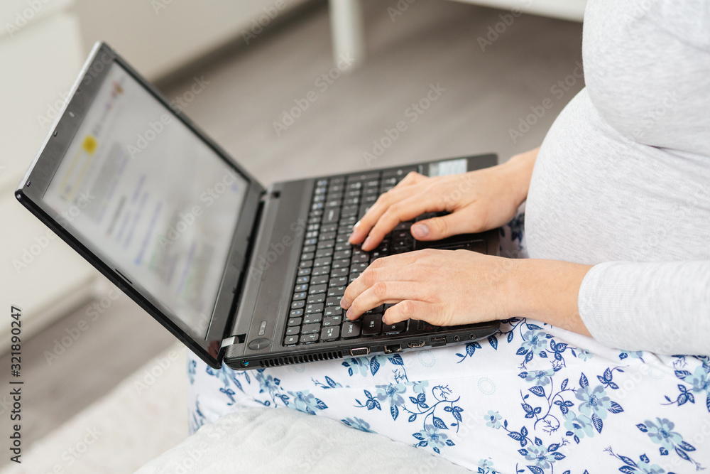 Fototapeta premium A pregnant woman uses a laptop. Hand and a notebook close-up. Concept of modern technologies and freelance. Top view
