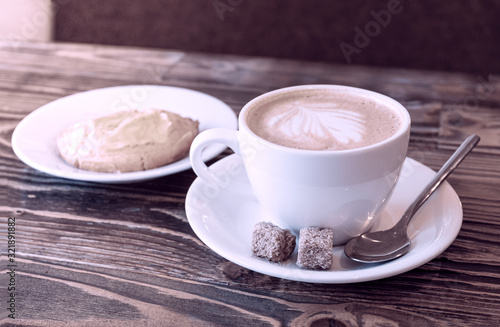 A cup with cappuccino and cookies with cottage cheese on a plate on a stocone with a wooden surface. Retro style. Horizontal orientation. Selective focus.