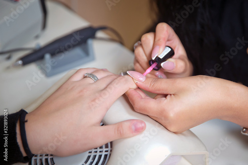 He paints his nails with white lacquer.Beautician painting client s nails with transparent lacquer during manicure process in a beauty salon. Concept . The master does a manicure in the salon .