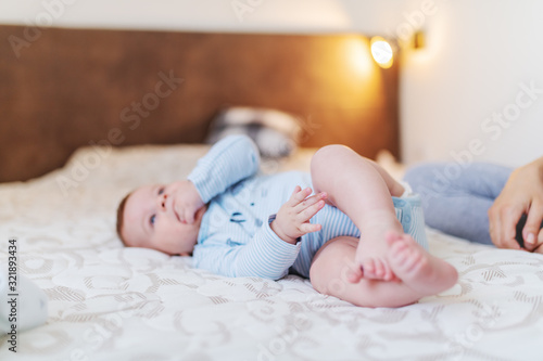 Wallpaper Mural Cute caucasian six months old baby boy dressed in bodysuit lying on bed in bedroom and sucking fingers. Next to him is mother. Torontodigital.ca