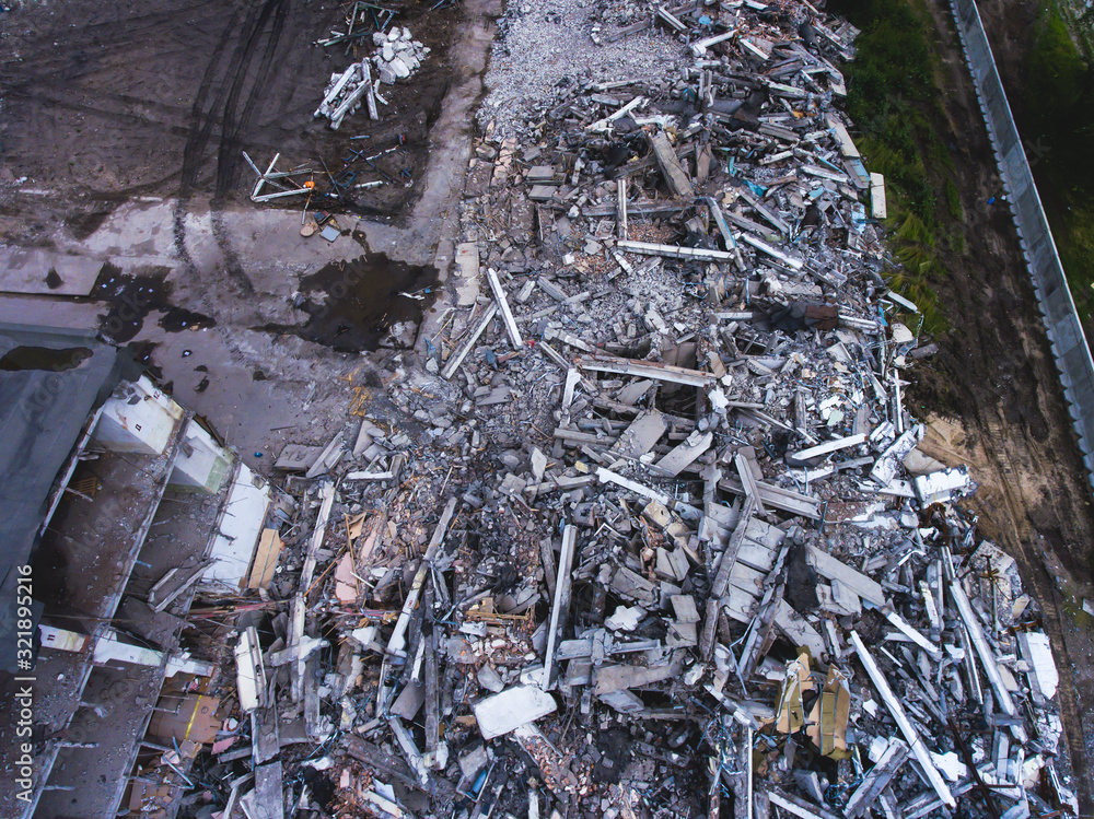 A process of buliding demolition, demolition site with heavy bulldozer and excavator with crushing equipment at work, demolished house, shot from air with drone