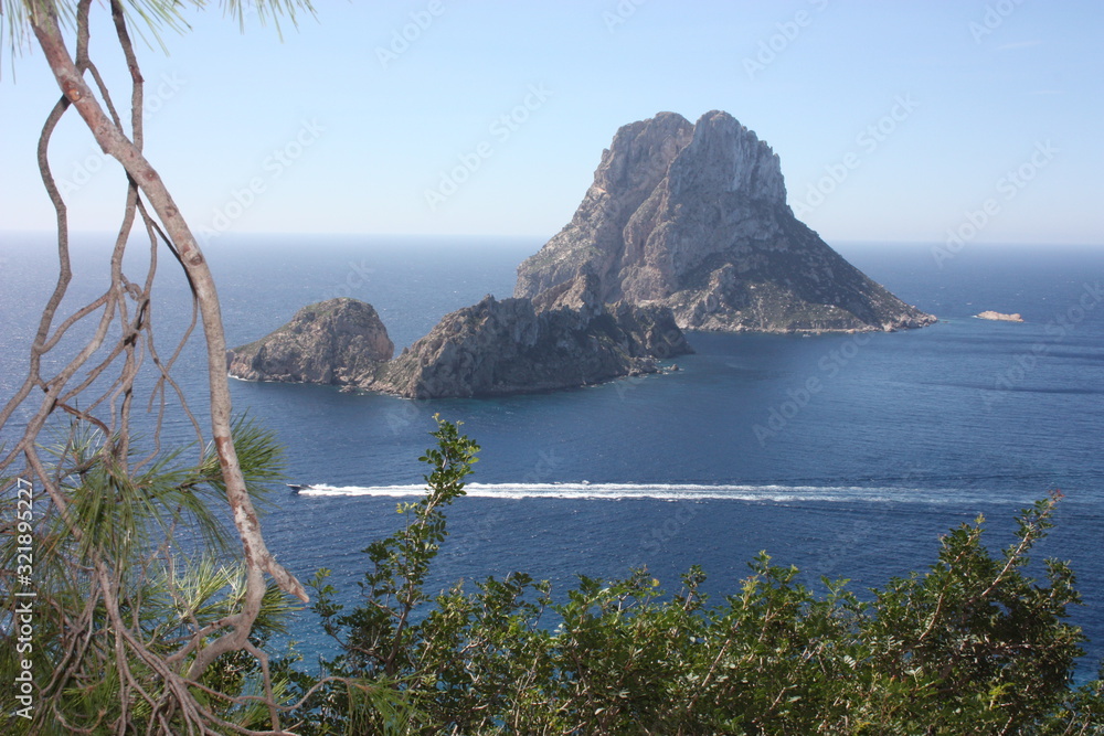 Fototapeta premium The magical island of Es Vedra with the small islet of Es Vedranell next to it in front of the coast of Cala d'Hort in the tourist island of Ibiza in the midst of nature between cliffs, beaches and co