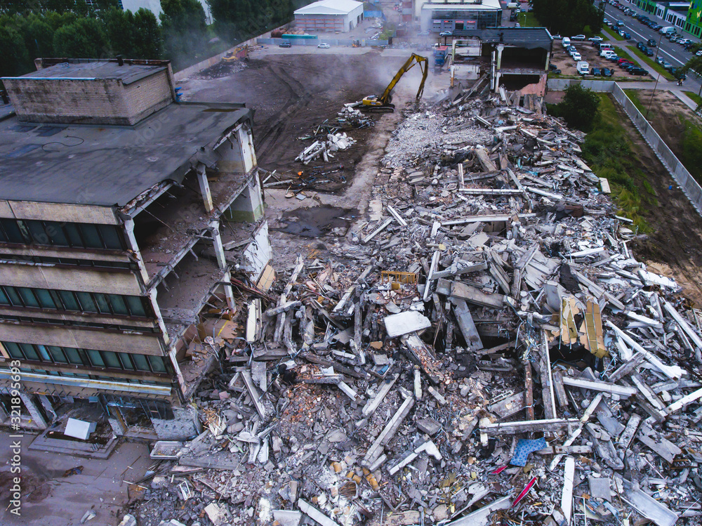 Obraz premium A process of buliding demolition, demolition site with heavy bulldozer and excavator with crushing equipment at work, demolished house, shot from air with drone