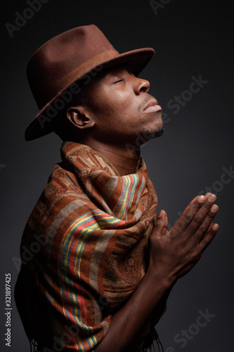 Studio portrait of an African man in a hat and poncho against a dark background.
