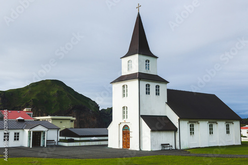 Church with Black roof and white walls in traditional nordic minimalist style on Vestmannaeyjar Heimaey island in Iceland. Simple architecture, green grass, nobody around.