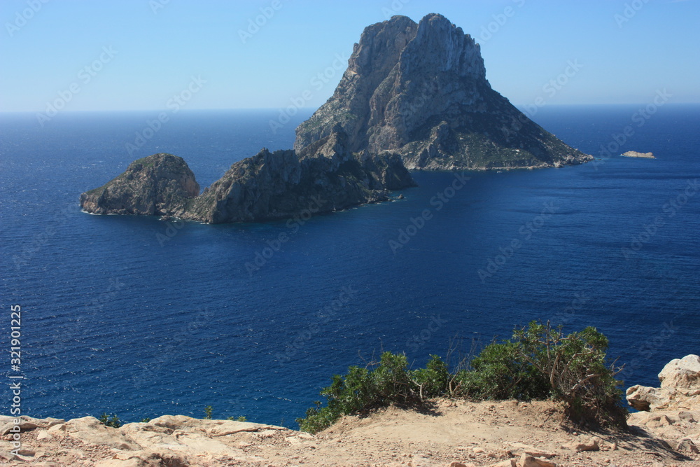Fototapeta premium The magical island of Es Vedra with the small islet of Es Vedranell next to it in front of the coast of Cala d'Hort in the tourist island of Ibiza in the midst of nature between cliffs,