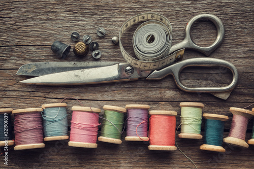 Row of vintage wooden spools of multicolored threads, tailoring scissors, thimbles, measuring tape, sewing items on wooden board. View from above. photo