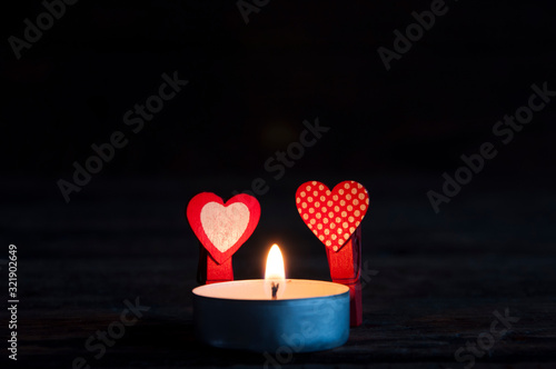 Little red clothespins hearts in the dark near a burning candle. Love