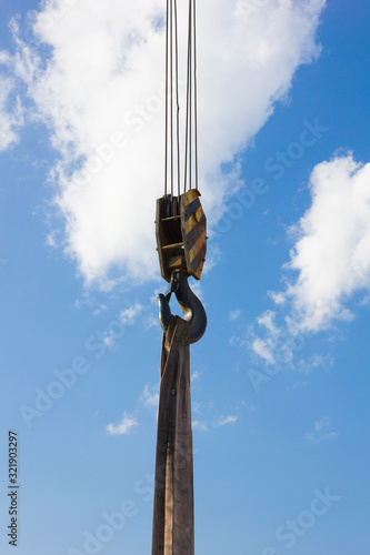 Black and yellow cargo crane hook with slings, against a blue sky with clouds