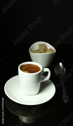Concetto di bevanda italiana. Tazza bianca classica di caffè espresso con caffè su fondo nero. Zollette di zucchero bruno sullo sfondo.