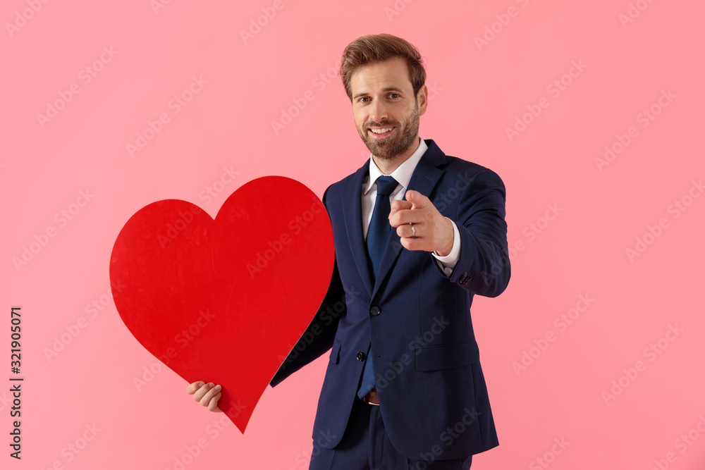 Cheerful businessman holding a heart shape and pointing forward Cheerful businessman holding a heart shape and pointing forward
