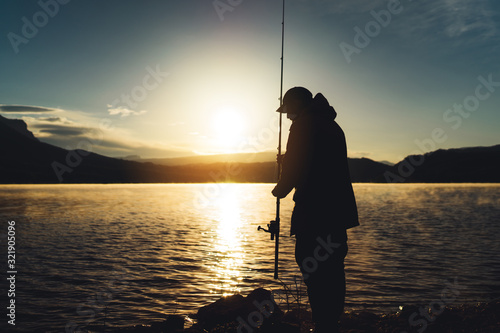 silhouette fisherman wirh fishing rod at sunrise sunlight, outline man enjoy hobby sport on evening lake, person catch fish on pond on background night sky, fishery concept