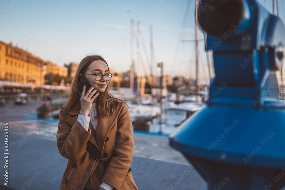 Traveler businesswoman calling mobile phone in evening sea port Barcelona. Smile girl tourist in glasses using smartphone technology online gadget cellphone. Digital communication on sunset