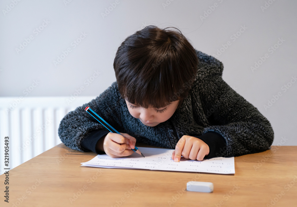 Portrait of school kid boy siting on table doing homework, Happy Child holding pencil writing, A boy writing English words on white paper, Elementary school and homeschooling concept Portrait of school kid boy siting on table doing homework, Happy Child holding pencil writing, A boy writing English words on white paper, Elementary school and homeschooling concept