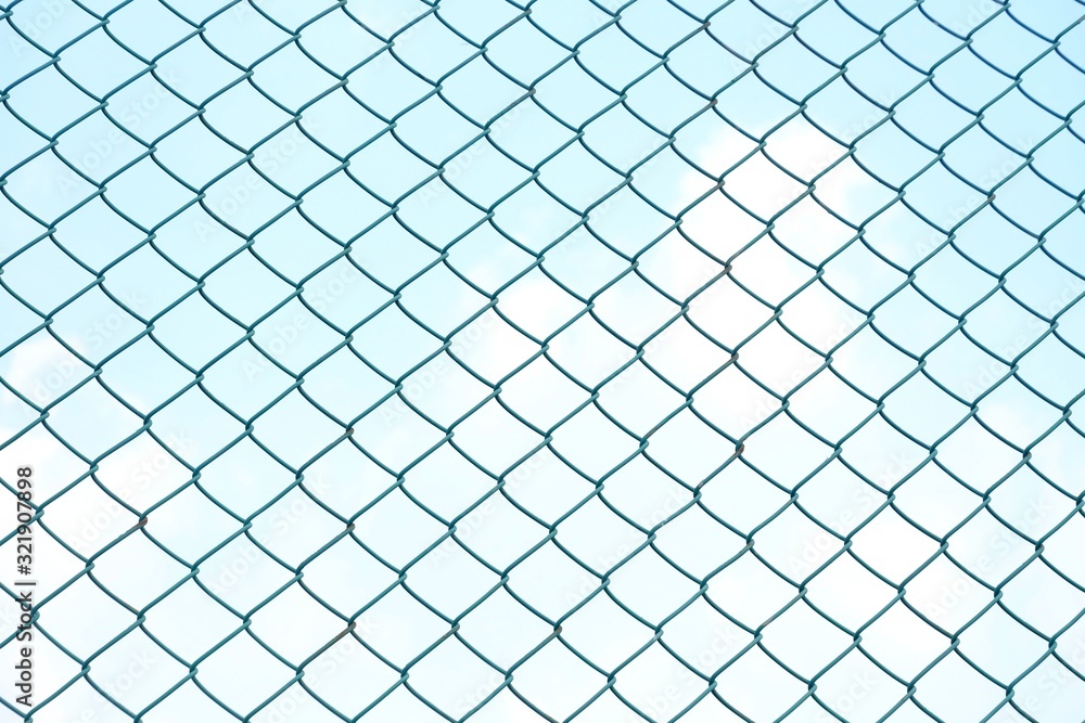 Close up green square wire mesh chain link fence against blue sky white clouds for background texture Close up green square wire mesh chain link fence against blue sky white clouds for background texture