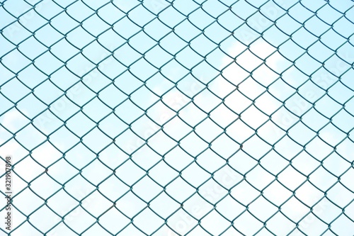 Close up green square wire mesh chain link fence against blue sky white clouds for background texture