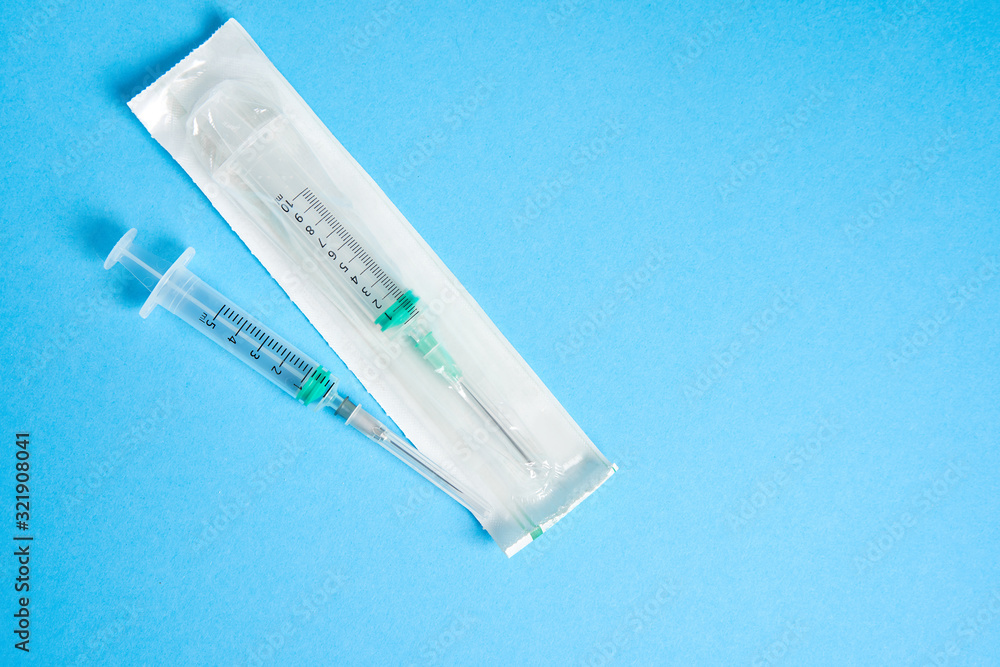 Obraz premium Two plastic disposable medical syringes open and package lie on blue background.
