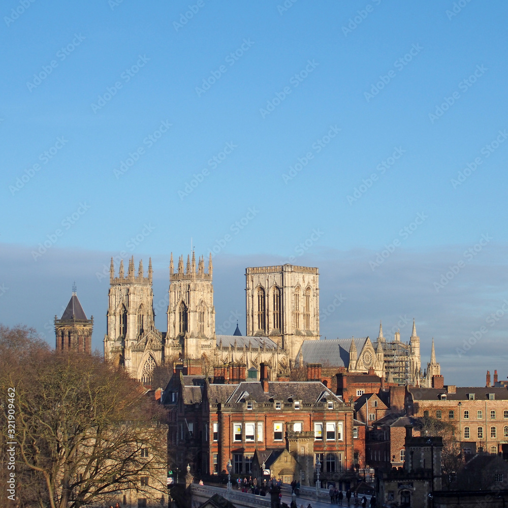 a view of york minster from the city walls with people and traffic crossing lendal bridge