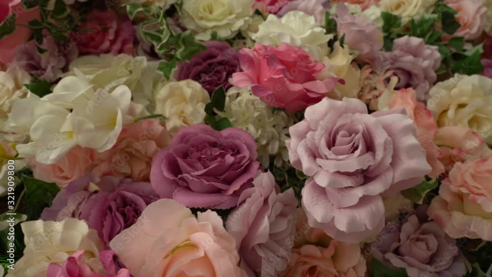 Closeup view of many artificial synthetic flowers of pastel red, pink, purple, white and orange colors.