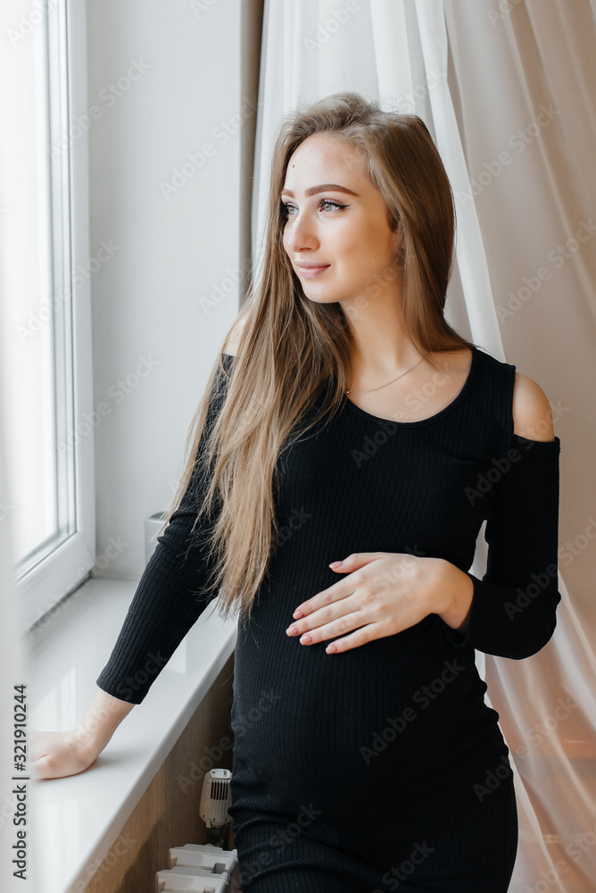 A beautiful pregnant girl is standing in a room near the window A beautiful pregnant girl is standing in a room near the window
