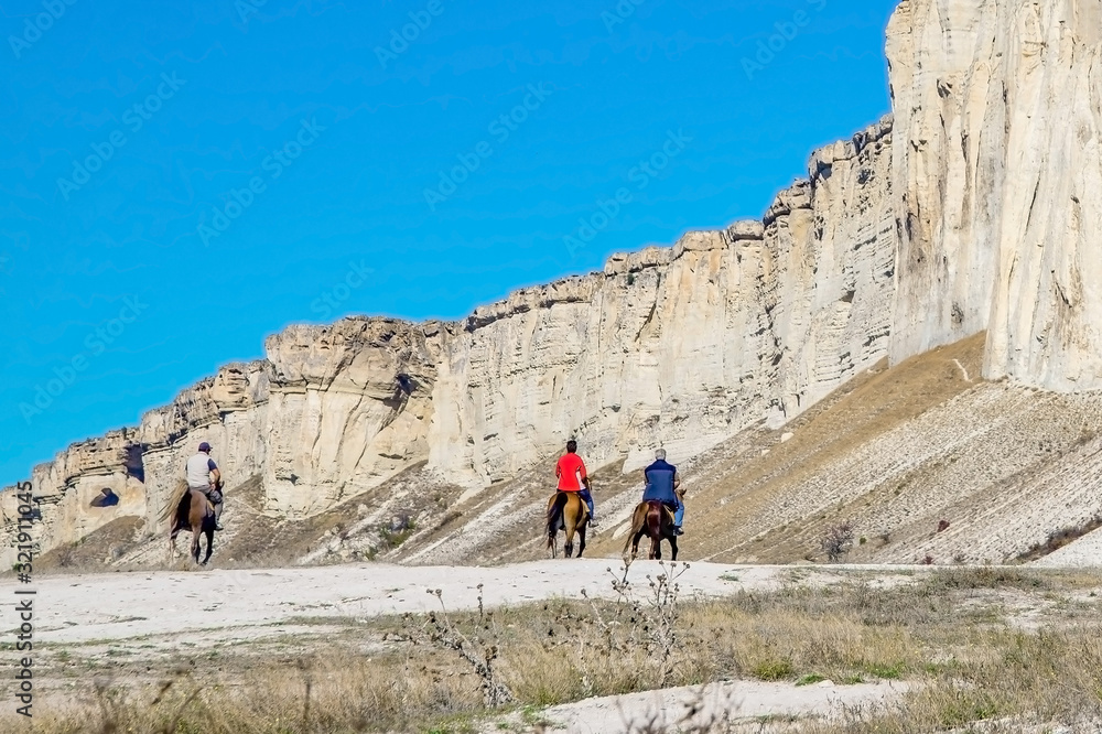 group of people walk on horseback on the background of rocky canyons