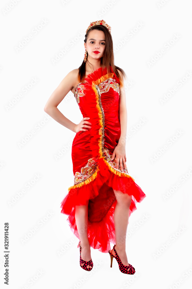 Beautiful brunette adult girl in a red silk chic, luxurious dress wearing gold with red stones crown standing and posing on white background. Isolate Beautiful brunette adult girl in a red silk chic, luxurious dress wearing gold with red stones crown standing and posing on white background. Isolate