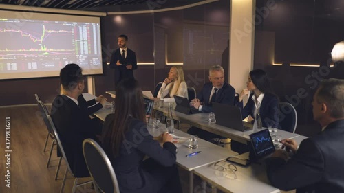 The businessman standing near the large screen and speaking