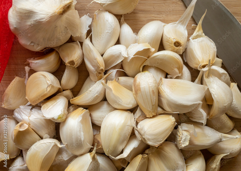 Many garlic cloves close up on a wooden cutting board with a knife.