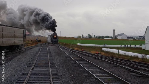 Head on View of a Steam Locomotive Pulling Freight Pulling into Yard with Smoke and Steam on a Rainy Day