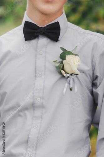 white roses flowers in buttonhole, the grooms friend is dressed in a grey shirt and a bow tie. Wedding day. Outfit of the day.