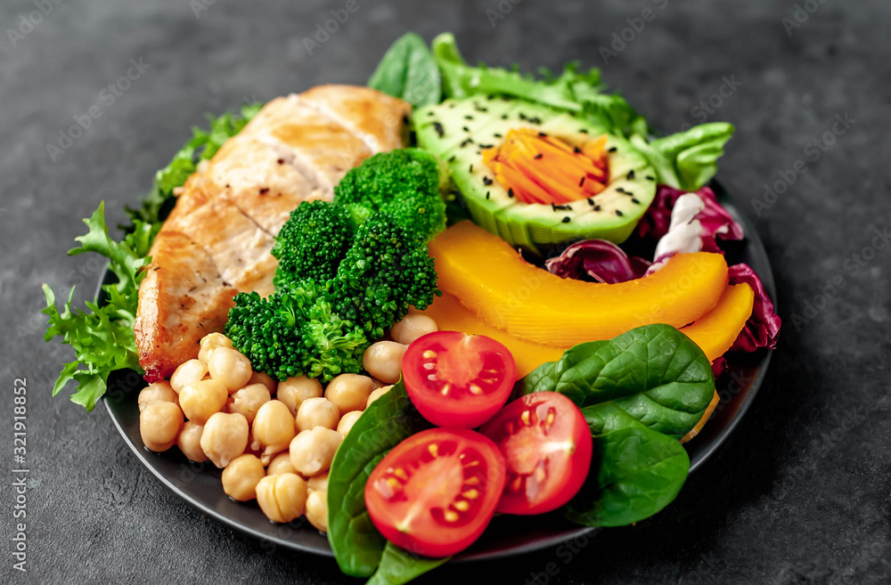 Bowl Buddha. chicken, broccoli, chickpeas, pumpkin, avocado, carrot, tomato, lettuce on a plate  on a stone background