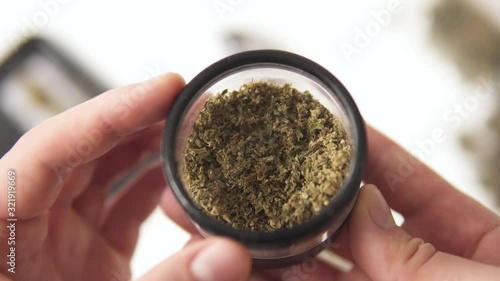 in hand a grinder to grind marijuana weed against a background of flowers of cannabis and scales and joint top view 