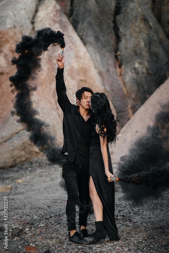 An Asian couple in love lit black smoke bombs in the mountains. Colored smoke